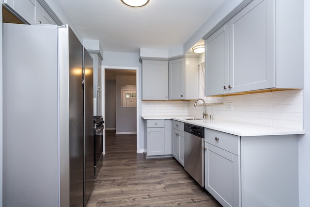 kitchen with decorative backsplash, appliances with stainless steel finishes, dark wood-type flooring, light countertops, and a sink