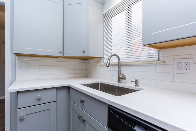 kitchen with a sink, light countertops, stainless steel dishwasher, gray cabinets, and decorative backsplash