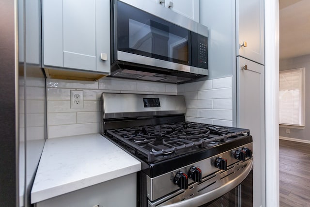 kitchen with stainless steel appliances, wood finished floors, backsplash, light stone countertops, and baseboards