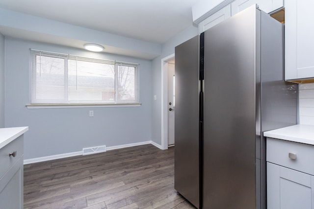 kitchen with dark wood-style flooring, visible vents, baseboards, light countertops, and freestanding refrigerator