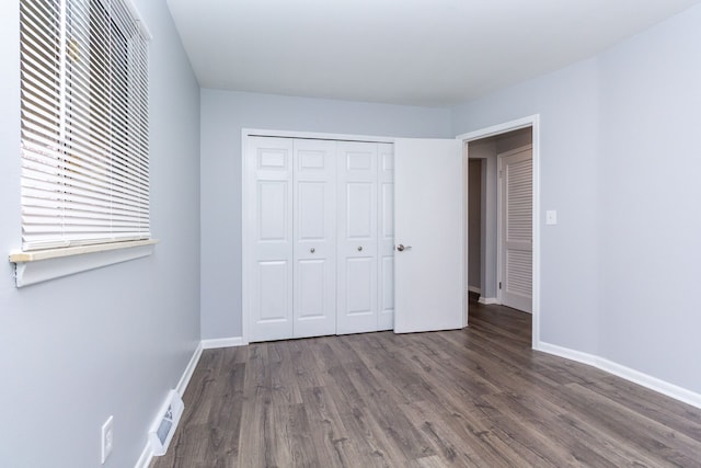 unfurnished bedroom with a closet, wood finished floors, visible vents, and baseboards