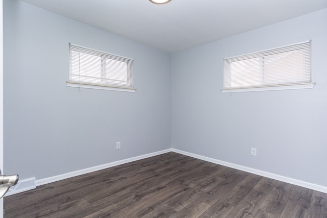 unfurnished room featuring dark wood-type flooring, visible vents, and baseboards