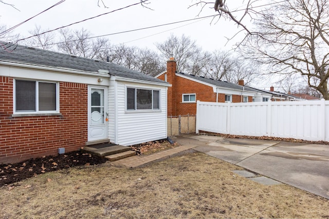 rear view of house featuring entry steps, roof with shingles, fence, a patio area, and brick siding