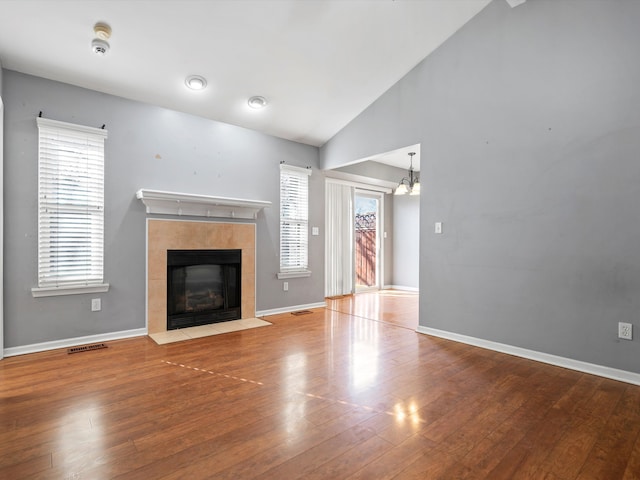 unfurnished living room featuring a fireplace, lofted ceiling, visible vents, wood finished floors, and baseboards