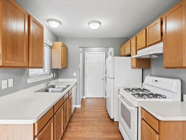 kitchen with white appliances, under cabinet range hood, light countertops, and a sink