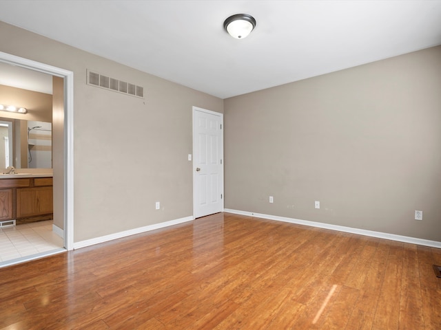 unfurnished bedroom featuring ensuite bathroom, light wood-style flooring, a sink, visible vents, and baseboards