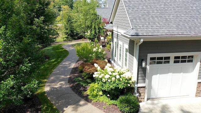 view of side of home featuring a garage, stone siding, and roof with shingles