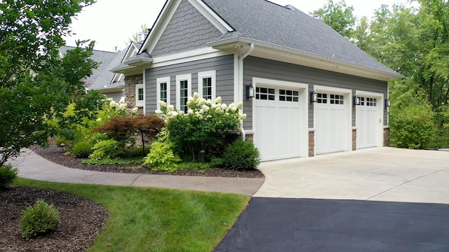 view of home's exterior with stone siding, roof with shingles, driveway, and an attached garage