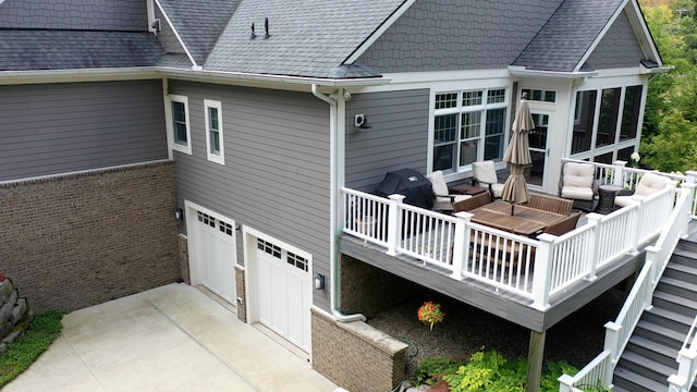 back of house featuring driveway, a shingled roof, a deck with water view, and an attached garage