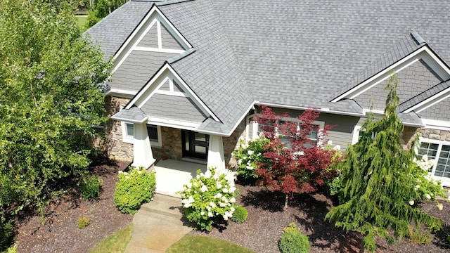 craftsman-style home featuring stone siding, a shingled roof, and covered porch