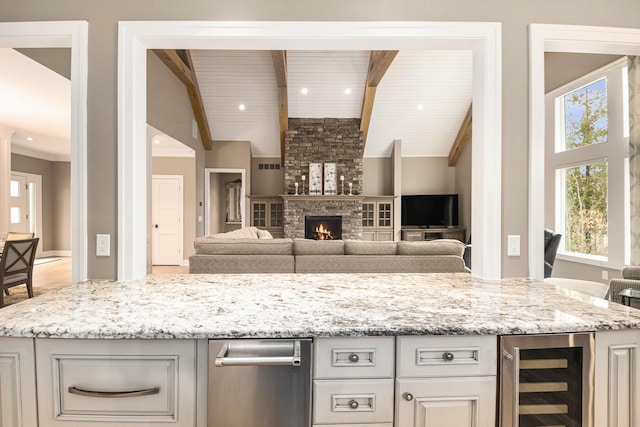 kitchen featuring a warm lit fireplace, wine cooler, open floor plan, light stone countertops, and beamed ceiling