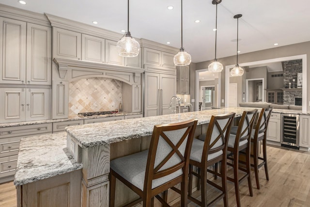 kitchen with wine cooler, stainless steel gas stovetop, backsplash, light wood-style flooring, and an island with sink