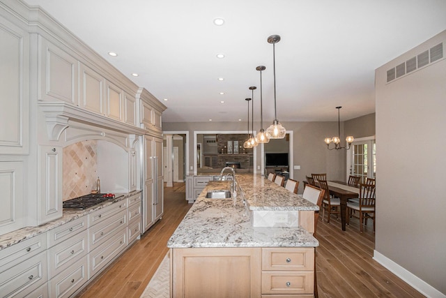 kitchen with tasteful backsplash, light wood-type flooring, a sink, and stainless steel gas stovetop