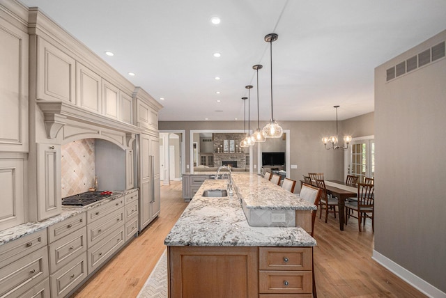 kitchen with cream cabinets, a sink, open floor plan, a brick fireplace, and a large island with sink