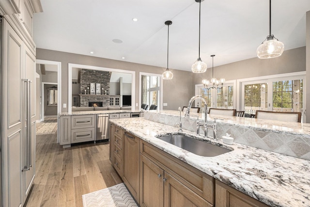 kitchen with light stone counters, wood finished floors, hanging light fixtures, a sink, and recessed lighting