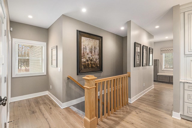 hall with light wood finished floors, an upstairs landing, and baseboards