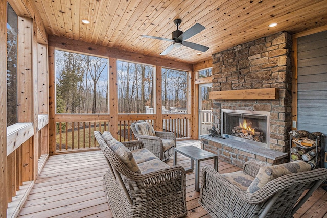 sunroom with ceiling fan, an outdoor stone fireplace, and wood ceiling