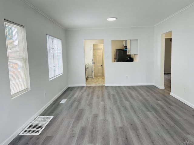 unfurnished room with baseboards, light wood-style flooring, visible vents, and crown molding