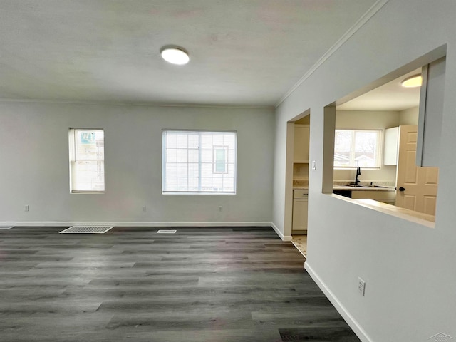 empty room with dark wood-style floors, visible vents, crown molding, and baseboards