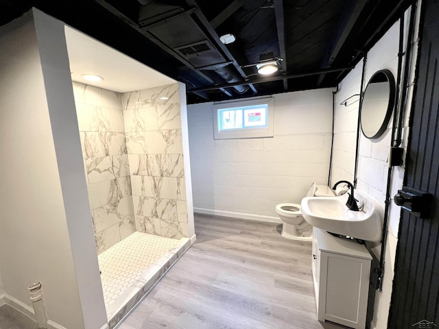 full bathroom featuring toilet, a tile shower, vanity, wood finished floors, and baseboards