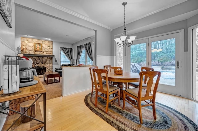 dining space featuring a wainscoted wall, ornamental molding, a stone fireplace, light wood-style flooring, and an inviting chandelier