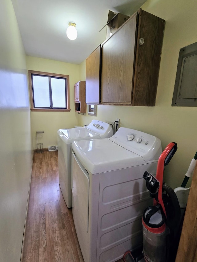 laundry room with washing machine and dryer, wood finished floors, visible vents, cabinet space, and electric panel