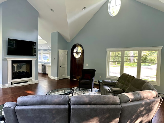 living area with dark wood-style floors, high vaulted ceiling, a glass covered fireplace, and baseboards