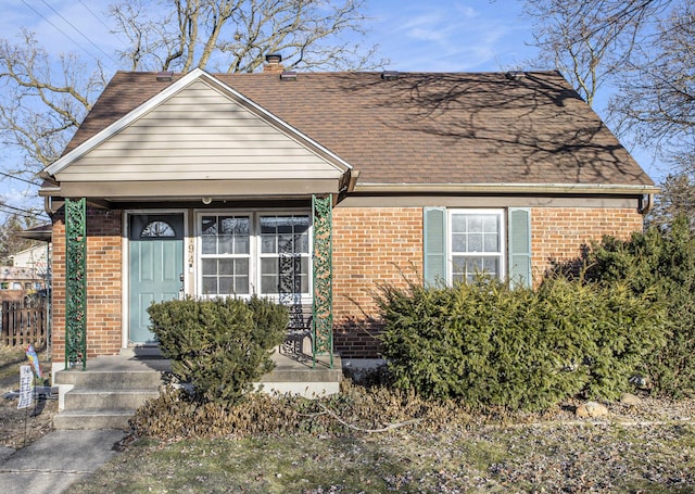 view of front facade with roof with shingles, a chimney, and brick siding