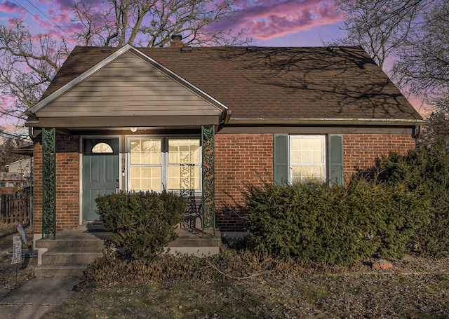 view of front facade with brick siding and roof with shingles