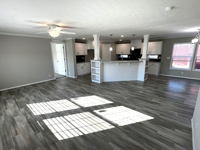 unfurnished living room featuring crown molding, decorative columns, ceiling fan with notable chandelier, a textured ceiling, and dark wood-style flooring