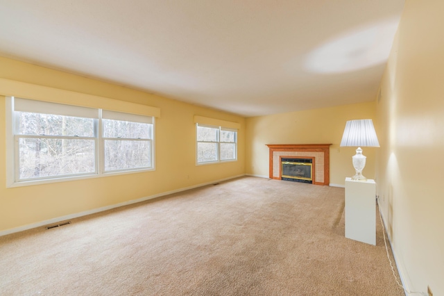 unfurnished living room featuring a tiled fireplace, carpet, visible vents, and baseboards