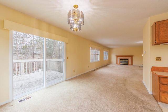 unfurnished living room with baseboards, visible vents, light colored carpet, a glass covered fireplace, and a notable chandelier