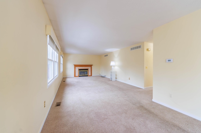 unfurnished living room featuring a tiled fireplace, carpet flooring, visible vents, and baseboards