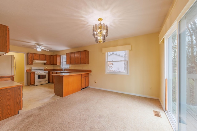 kitchen featuring brown cabinets, light colored carpet, a peninsula, white appliances, and under cabinet range hood