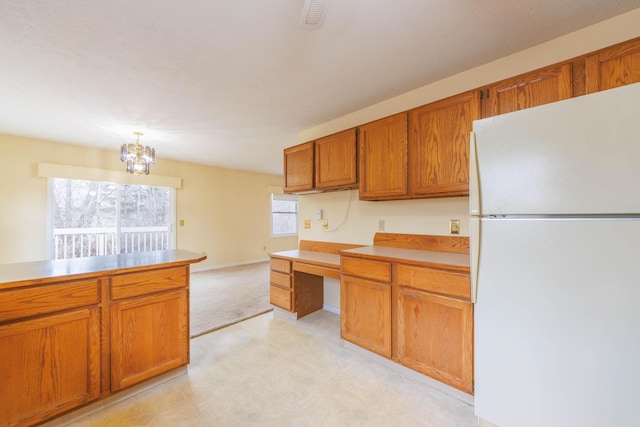 kitchen with light countertops, hanging light fixtures, built in study area, freestanding refrigerator, and brown cabinetry