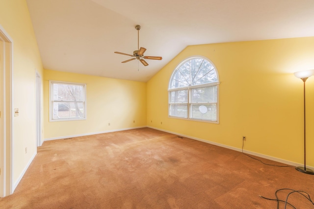 empty room with a ceiling fan, light colored carpet, vaulted ceiling, and baseboards