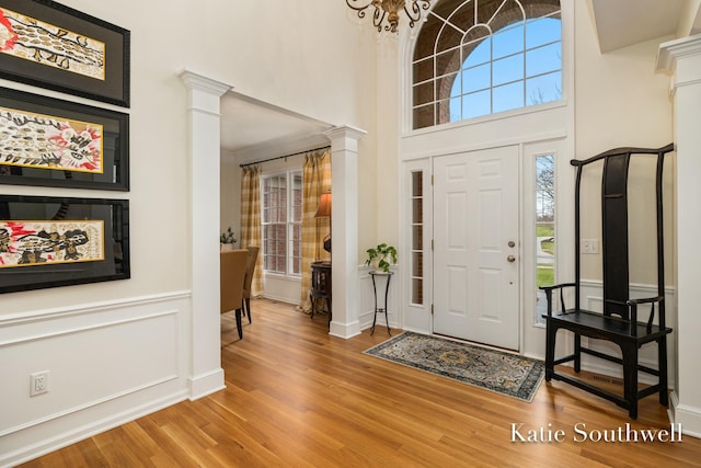 entryway with a towering ceiling, wood finished floors, decorative columns, and a decorative wall