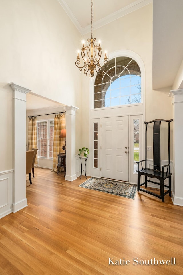 foyer with crown molding, a high ceiling, decorative columns, and light wood-style floors