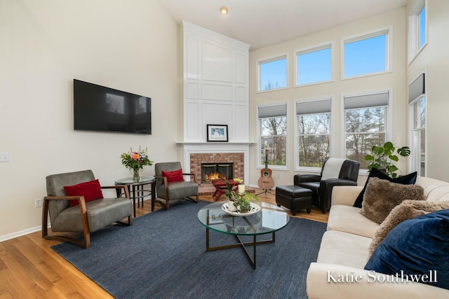 living room featuring a fireplace, a towering ceiling, baseboards, and wood finished floors