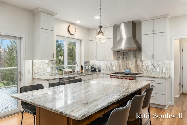 kitchen featuring wall chimney exhaust hood, a kitchen bar, white cabinetry, and a sink