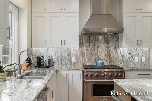 kitchen featuring a sink, wall chimney range hood, white cabinetry, backsplash, and luxury stove