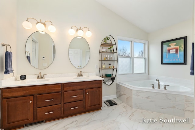 bathroom featuring marble finish floor, a garden tub, double vanity, lofted ceiling, and a sink