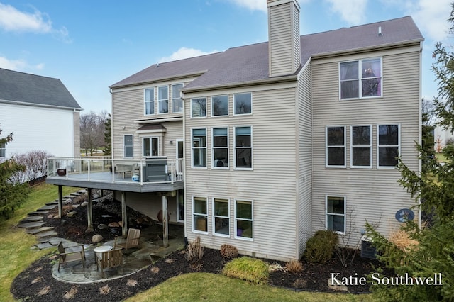 back of house featuring a deck, a patio, stairs, a lawn, and a chimney