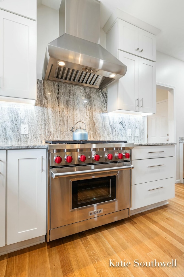 kitchen featuring light wood finished floors, designer stove, backsplash, white cabinets, and wall chimney exhaust hood