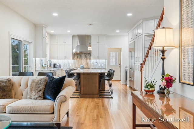 kitchen with light wood finished floors, tasteful backsplash, white cabinets, wall chimney exhaust hood, and open floor plan