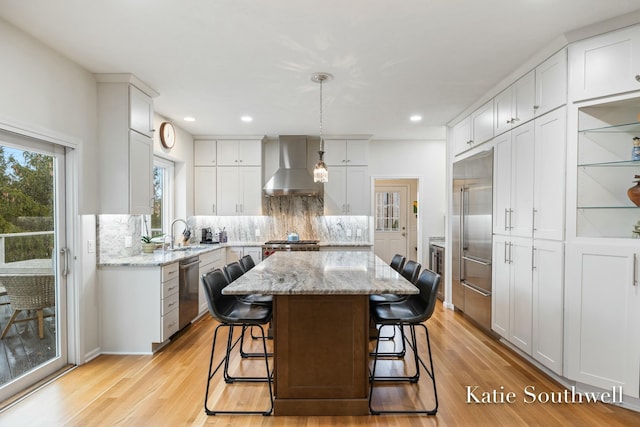 kitchen featuring light wood finished floors, decorative backsplash, a center island, stainless steel appliances, and wall chimney range hood