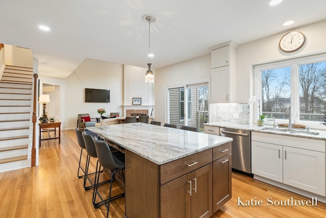 kitchen featuring dishwasher, light wood-style flooring, a breakfast bar, white cabinetry, and a sink