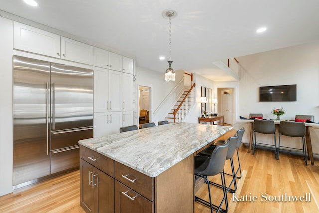 kitchen featuring light stone counters, white cabinets, stainless steel built in fridge, and light wood-style flooring