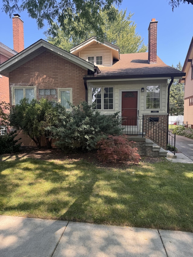 view of front of house with brick siding, a chimney, and a front lawn