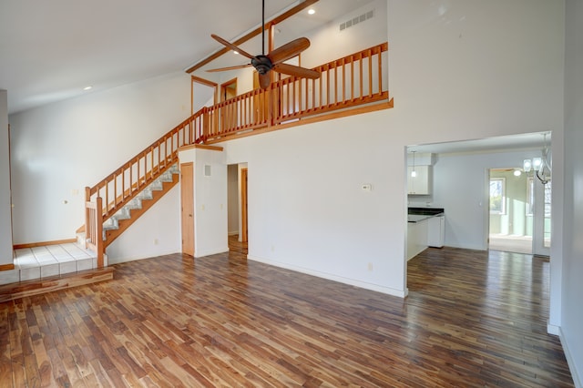 unfurnished living room featuring ceiling fan with notable chandelier, wood finished floors, a high ceiling, and stairs